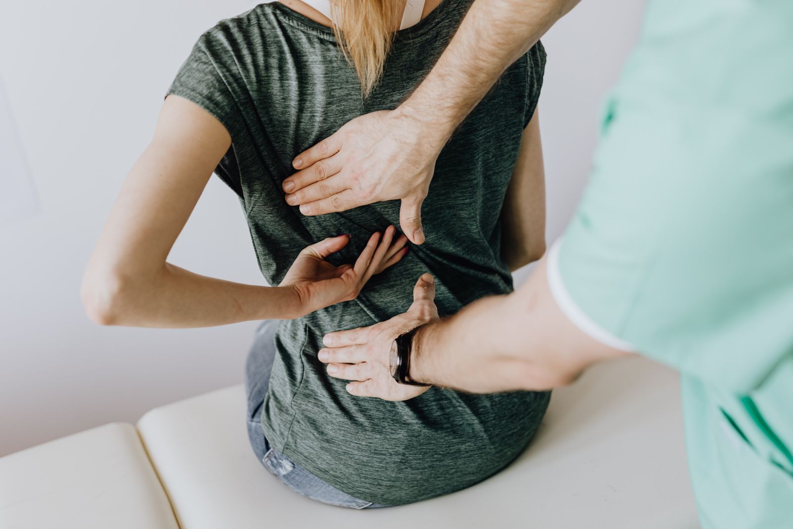 Physiotherapist's hands assessing a woman's painful mid-back during a clinical movement assessment